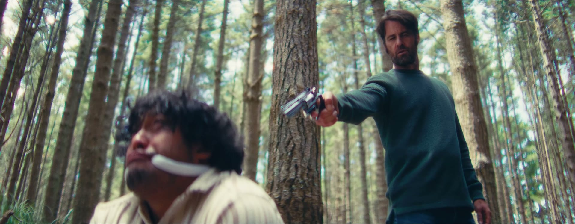Armed man confronting a seated man in a forest