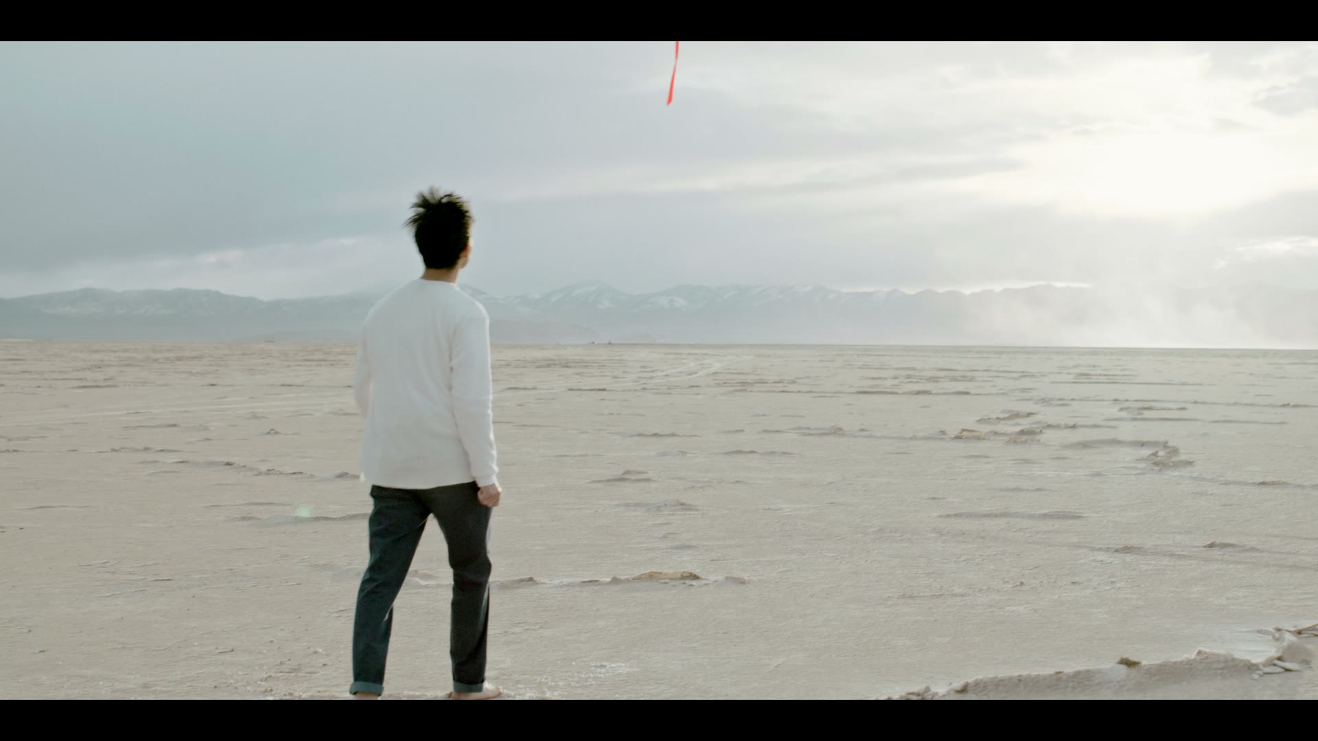 A man on a white salt flat watching a red streak fall from the sky